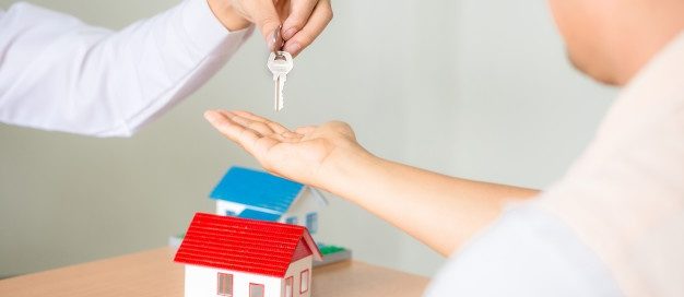 Landlord handing over house keys to a tenant with a small house model on the table, symbolizing rental property management and eviction guidelines in Texas.