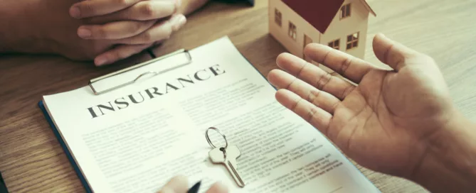 Person reviewing a landlord insurance contract with house model and keys on desk