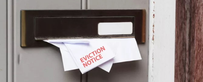 Eviction notice with red text partially inserted in a brass mail slot on a worn wooden door, symbolizing urgency and distress.