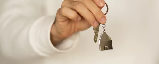 Hands exchanging a pen over a rental lease agreement with house keys on the table.