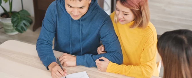 Couple signing documents at table with third person, suggesting positive agreement, for Dallas-Fort Worth landlord insurance explained.