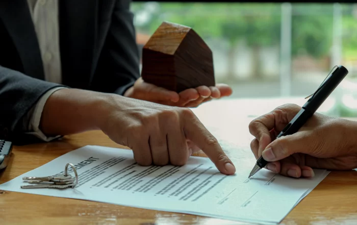 Two hands over contract with pen, wooden house and keys, illustrating landlord-tenant law myths and misconceptions.