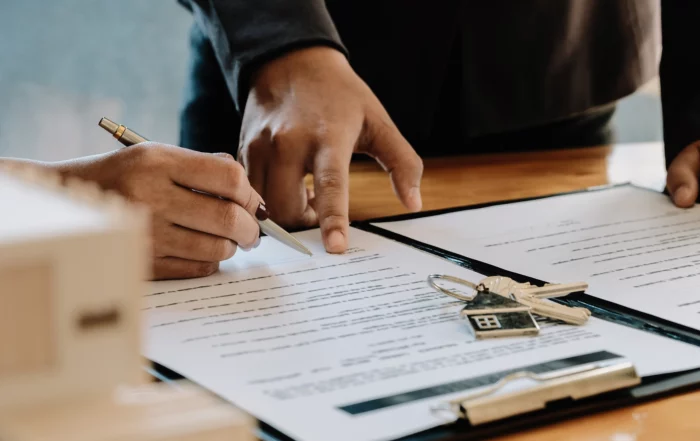 Two hands over a contract with pen and house keychain, illustrating landlord-tenant mediation vs litigation in Dallas-Fort Worth.